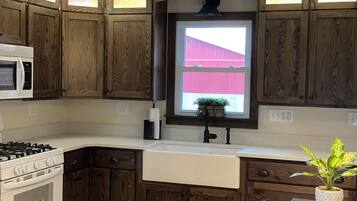 A kitchen with wooden cabinets, a microwave, a stove, a sink, and a window with a view of a red building.