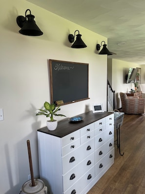 Una habitación con un aparador blanco, una pizarra con la palabra 'Welcome' escrita y una planta en maceta.