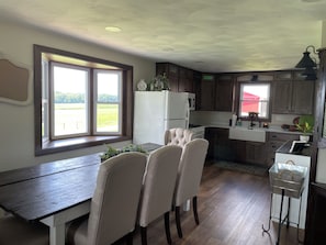 Een keuken met een eettafel, stoelen, een koelkast, magnetron en kastjes.