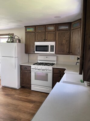 A kitchen with wooden cabinets, a white refrigerator, a microwave, and a stove. - Enjoy a stay on the farm by Lake Wilhelm and Goddard State Park in Sandy Lake PA (Sandy Lake)