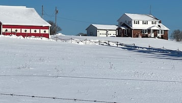 A snow-covered landscape with a barbed wire fence, a red building, and a white house with a garage.