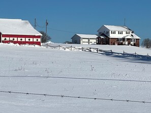 A snow-covered landscape with a barbed wire fence, a red building, and a white house with a garage.