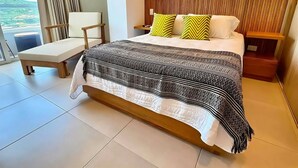 Moderni hotellihuone, jossa on suuri sänky, yöpöytä, tuoli ja näkymä ulos.
