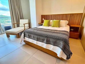 Habitación de hotel moderna con una cama grande, una mesita de noche, una silla y vistas al exterior.