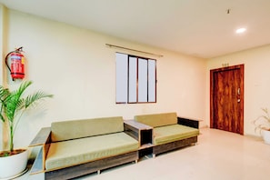A room with a sofa, a potted plant, a fire extinguisher, a window, and a wooden door. - Townhouse Nampally Metro Station Hyd (Hyderabad)