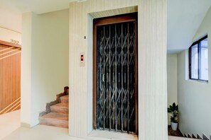 An elevator with a metal grille door, a digital display, and a staircase with wooden steps. - Townhouse Nampally Metro Station Hyd (Hyderabad)