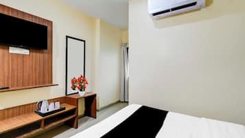 Habitación de hotel con cama, televisor montado en la pared, espejo, mesita con un florero y equipo de aire acondicionado.