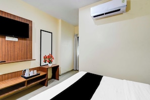 Habitación de hotel con cama, televisor montado en la pared, espejo, mesita con un florero y equipo de aire acondicionado.
