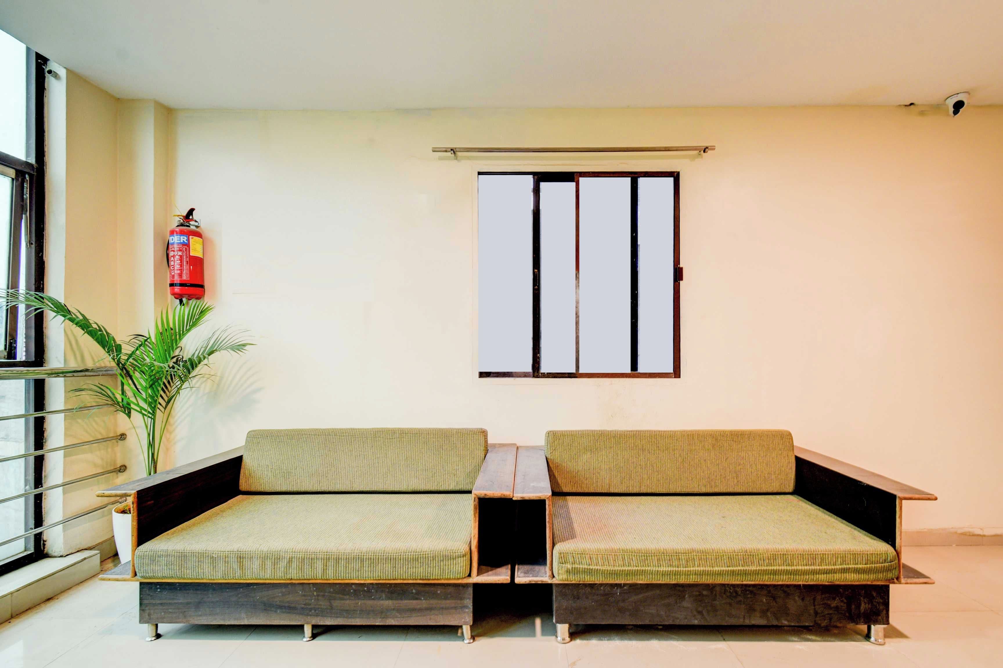 Ein Zimmer mit zwei grünen gepolsterten Sofas, einem kleinen Tisch, einer Topfpflanze, einem Feuerlöscher und einem Fenster mit Metallrahmen.