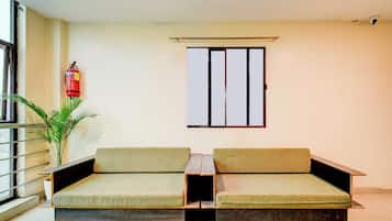 Ein Zimmer mit zwei grünen gepolsterten Sofas, einem kleinen Tisch, einer Topfpflanze, einem Feuerlöscher und einem Fenster mit Metallrahmen.