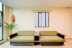 Una habitación con dos sofás verdes acolchados, una mesita, una planta en maceta, un extintor y una ventana con marco de metal.