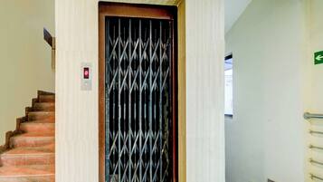 A staircase leading to a door with a metal security gate, a red emergency exit sign, and a wall-mounted light switch.
