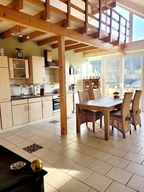 A spacious kitchen with wooden beams, a dining area with wicker chairs, and large windows offering a view of the outdoors. - Apartment "Panorama" with Mountain View, Wi-Fi, and Air Conditioning (Bad Neuenahr-Ahrweiler)