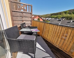 A balcony with wicker furniture, a table with a magazine, and a view of houses in the background. - Apartment "Panorama" with Mountain View, Wi-Fi, and Air Conditioning (Bad Neuenahr-Ahrweiler)