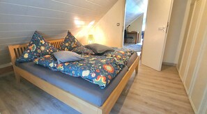 A bed with a floral-patterned bedspread and pillows, a wooden headboard, and a lamp on the wall. - Apartment "Panorama" with Mountain View, Wi-Fi, and Air Conditioning (Bad Neuenahr-Ahrweiler)