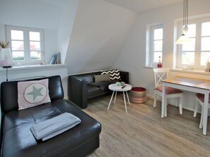 Un salon moderne avec un canapé en cuir noir, une table blanche et un fauteuil rouge. Il y a une fenêtre avec des cadres blancs et un luminaire suspendu.