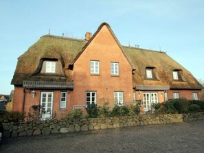 Une maison à deux étages, dotée d’un toit à forte pente, d’un mur en pierre à l’avant et d’une allée gravillonnée.
