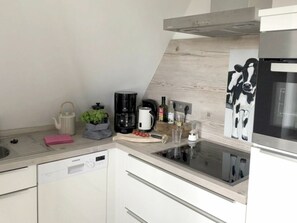 Une cuisine moderne équipée d’un lave-vaisselle, d’une machine à café, d’une bouilloire et d’un moulin à café, le tout posé sur le plan de travail.