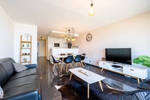 Ein modernes Wohnzimmer mit Sofa, Couchtisch, Essbereich und Fernseher.
