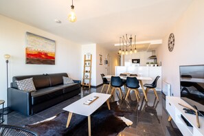 Ein modernes Wohnzimmer mit einem schwarzen Ledersofa, einem weißen Couchtisch und einem Essbereich mit Holzsesseln.
