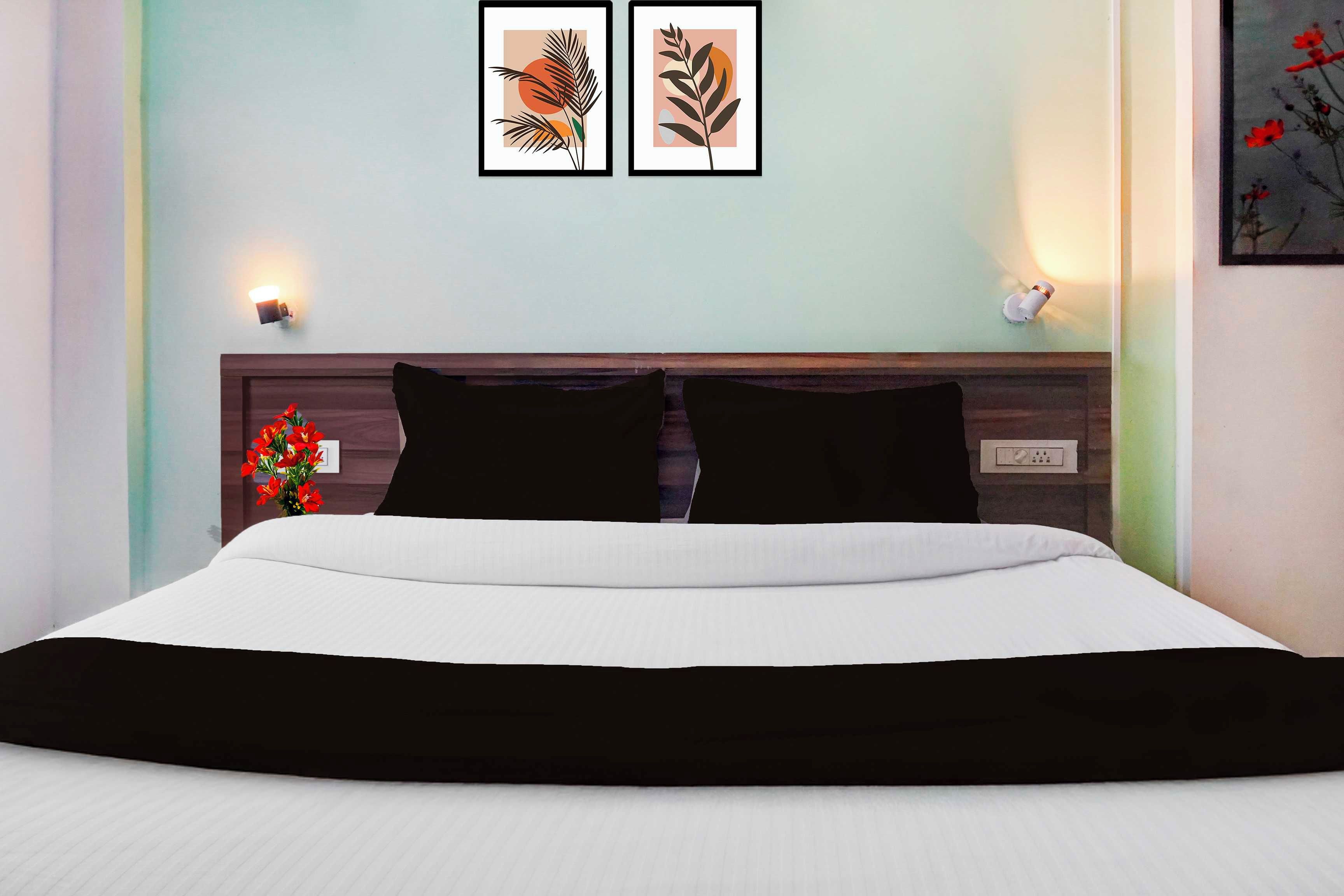 A hotel room with a bed, a nightstand, a wall-mounted light, and two framed artworks above the bed.