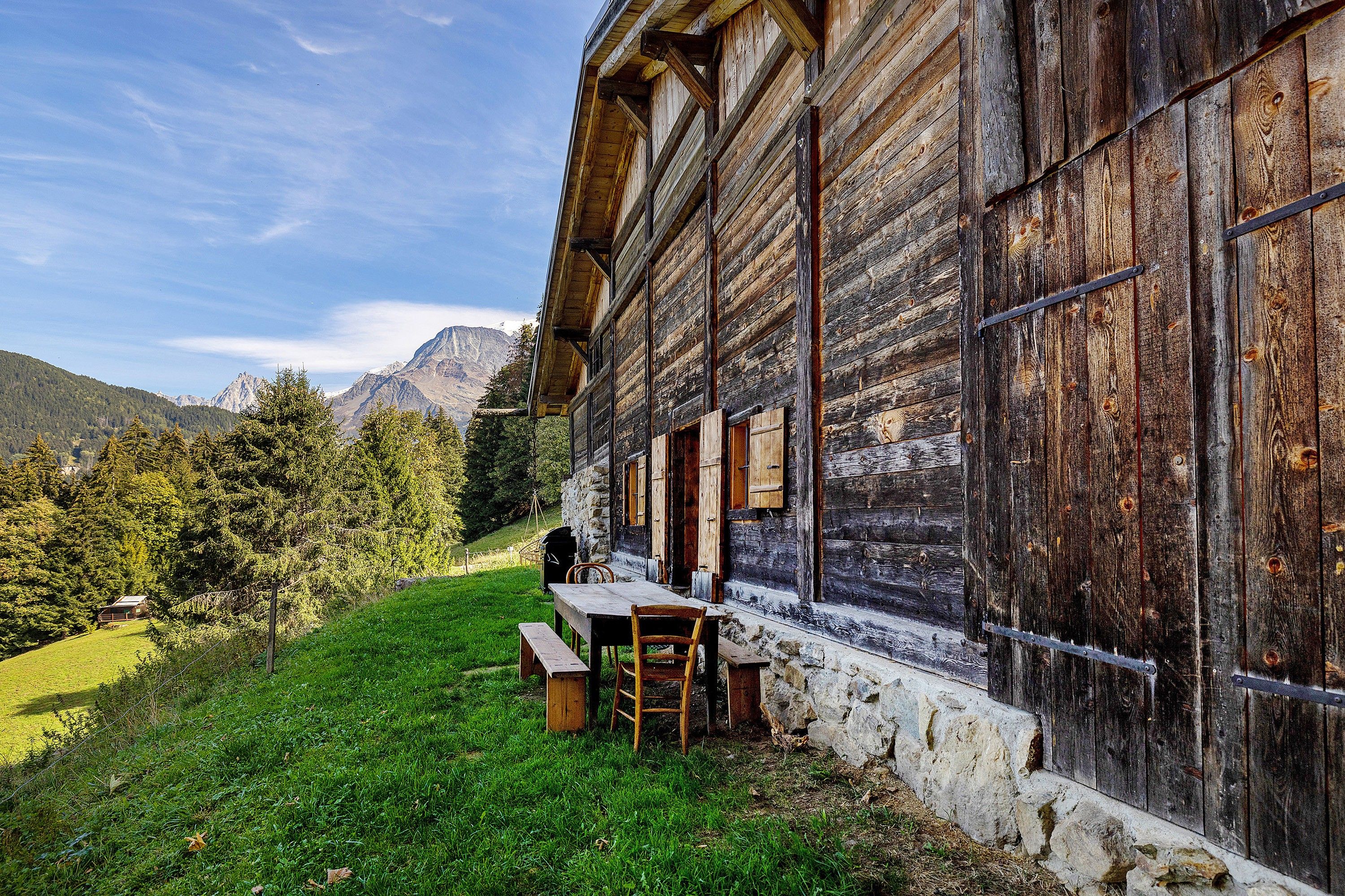 A rustic wooden building with a stone foundation, a bench, and a table outside.