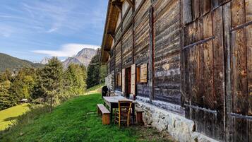 A rustic wooden building with a stone foundation, a bench, and a table outside.