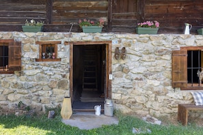 Un edificio rustico in pietra con una porta in legno, una piccola finestra con persiane e un cartello con un numero sopra la porta.