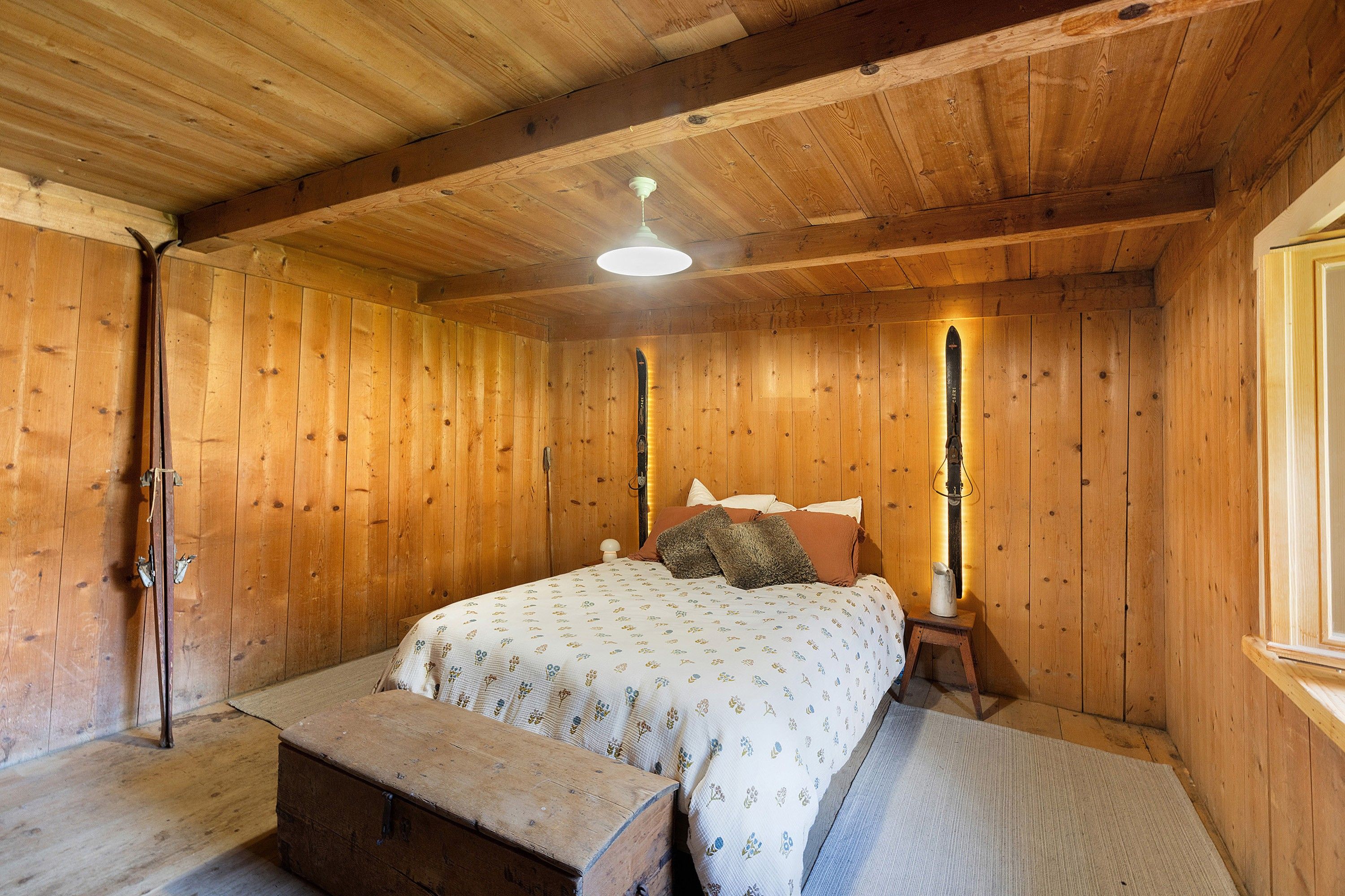 A wooden room with a bed, a bench, and a window.