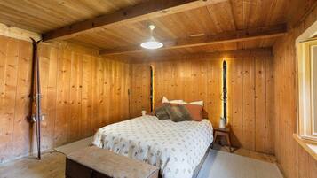 A wooden room with a bed, a bench, and a window.