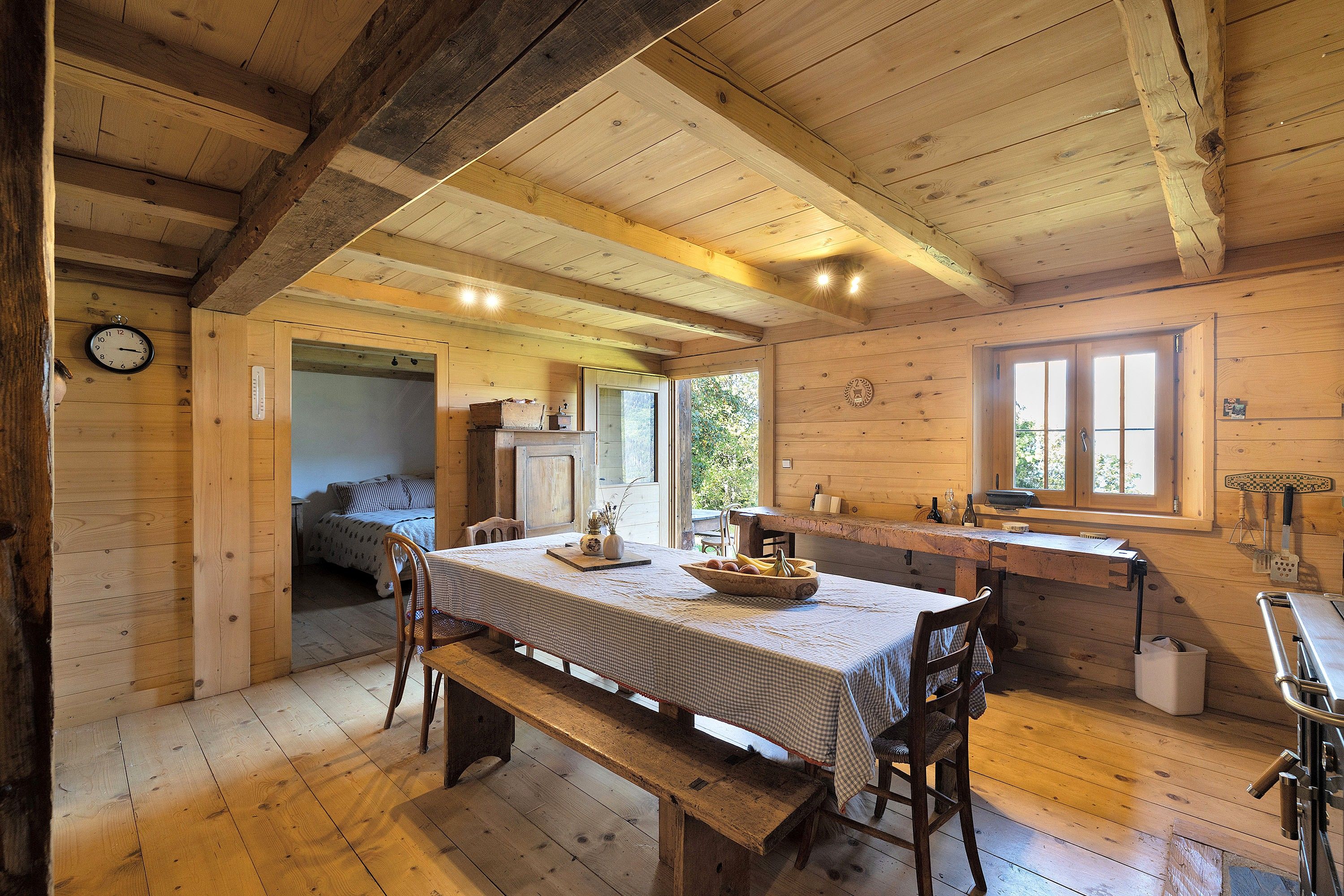 Un intérieur en bois comprenant une table à manger, des bancs, une horloge et une fenêtre.