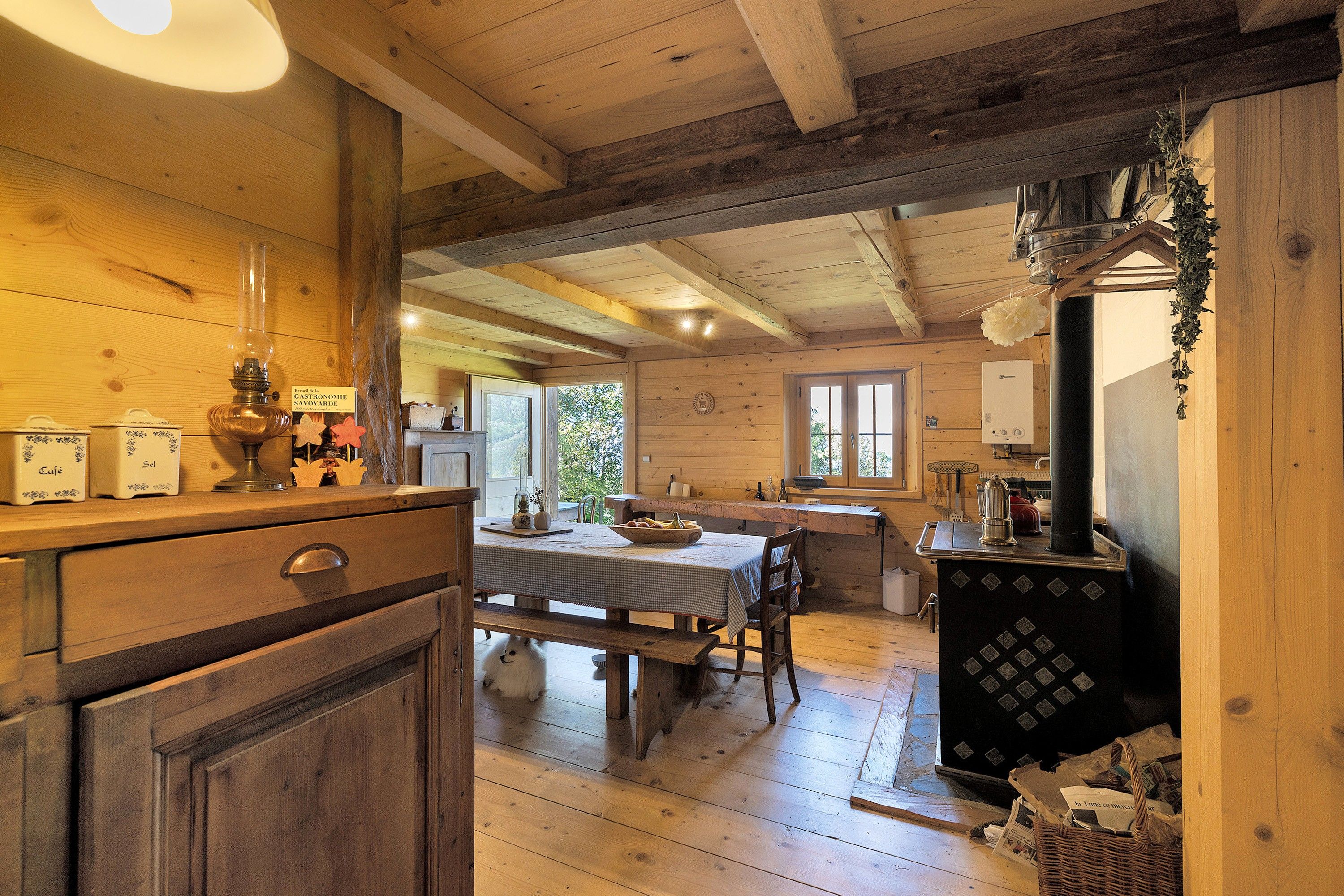 A rustic wooden interior with a dining area, wooden cabinets, and a traditional stove.