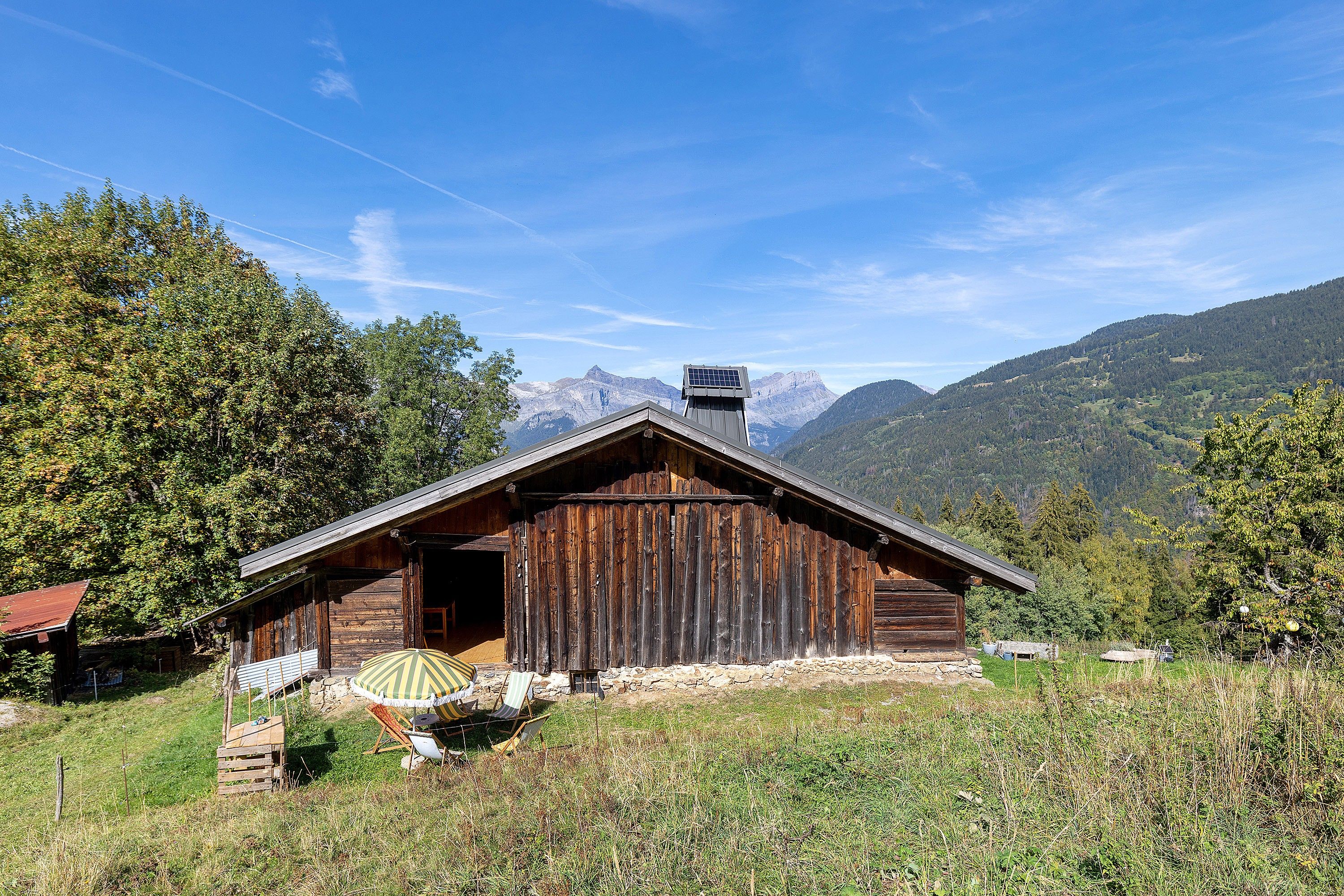 Un rustico chalet in legno con tetto spiovente, un camino e un piccolo portico con un ombrellone a righe.