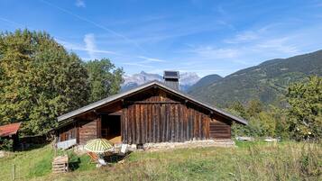 Un rustico chalet in legno con tetto spiovente, un camino e un piccolo portico con un ombrellone a righe.