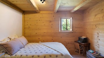 Une pièce en bois avec un lit, une petite table sur laquelle sont posés des livres, une fenêtre et un luminaire au plafond.