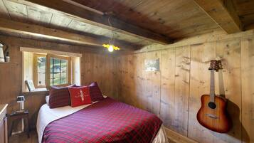 A wooden cabin room with a bed, a guitar, and a window.