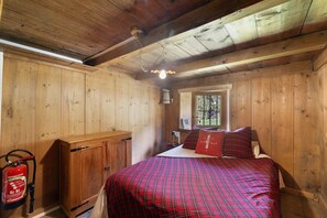 Camera da letto in una baita di legno, con un letto, un comodino, una cassettiera e una finestra.