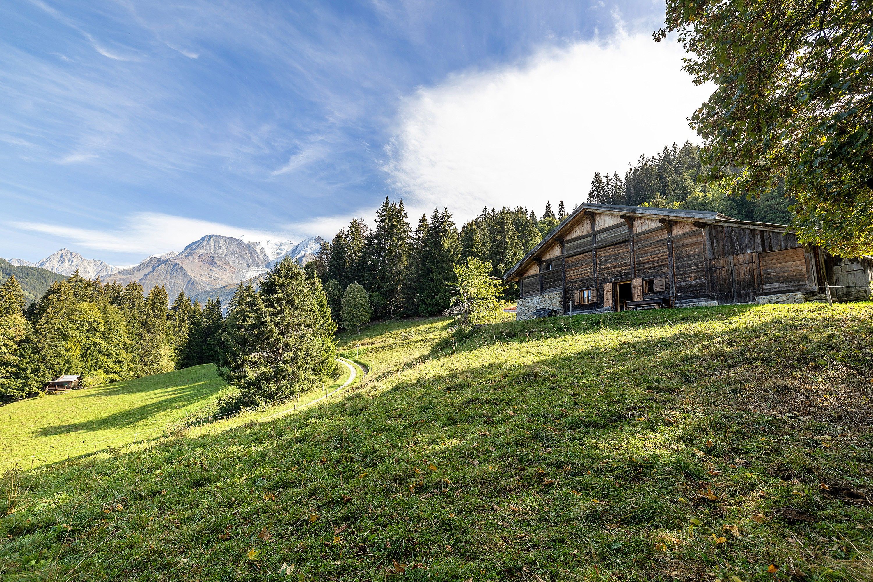 Eine rustikale Holzhütte mit Steinuntergrund, umgeben von üppigem Grün und einer Bergkulisse.