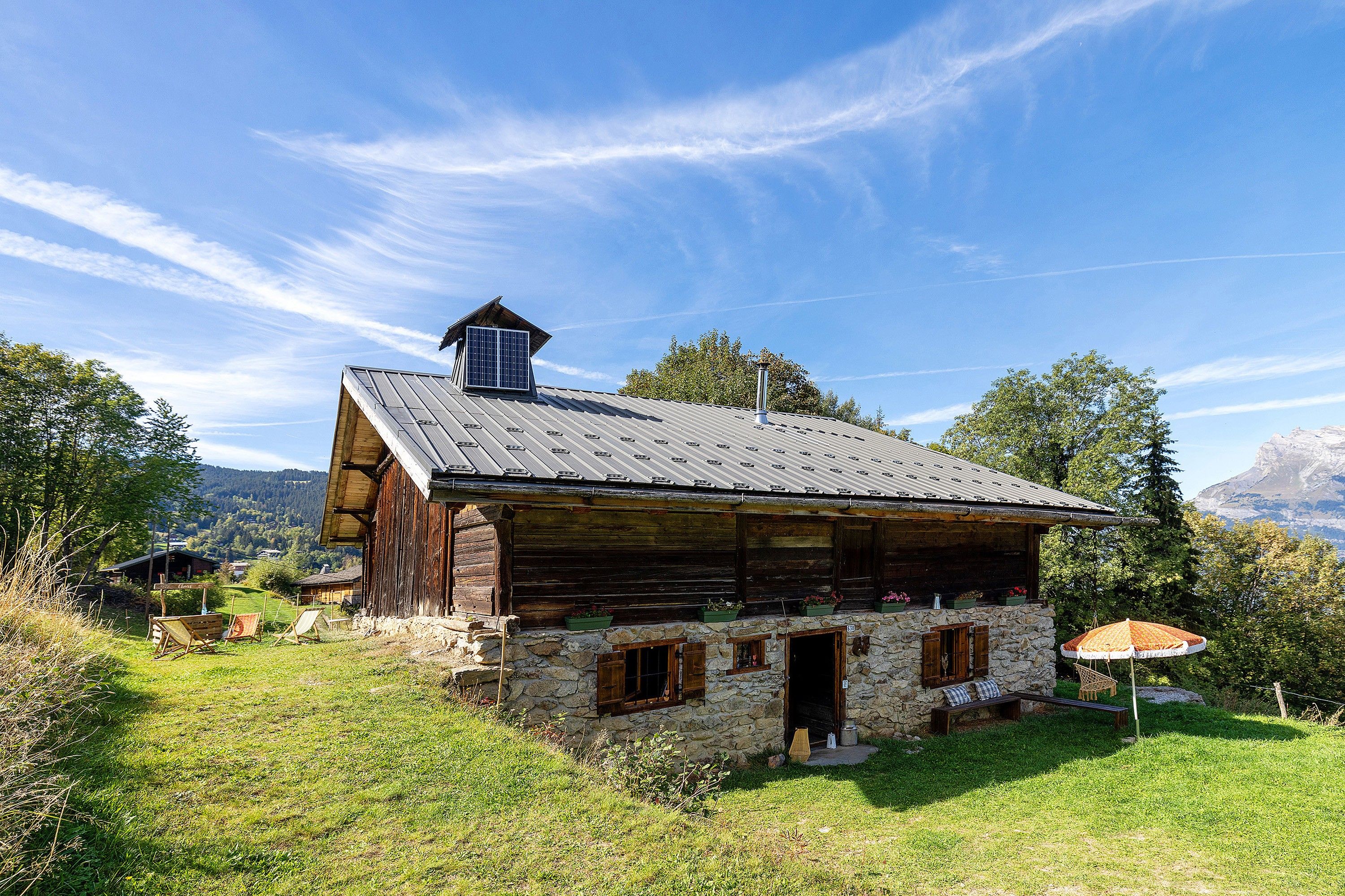 Un rustico chalet in legno con fondamenta in pietra, un camino e un piccolo portico con posti a sedere.