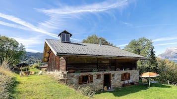 Un rustico chalet in legno con fondamenta in pietra, un camino e un piccolo portico con posti a sedere.