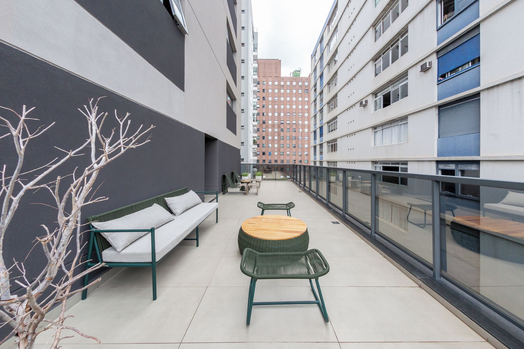 Uma área de estar moderna ao ar livre, com um sofá, cadeiras e uma mesa redonda, cercada por um parapeito de vidro.