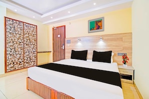 Habitació d'hotel amb llit, una taula de nit, un televisor penjat a la paret i un panell decoratiu a la paret.