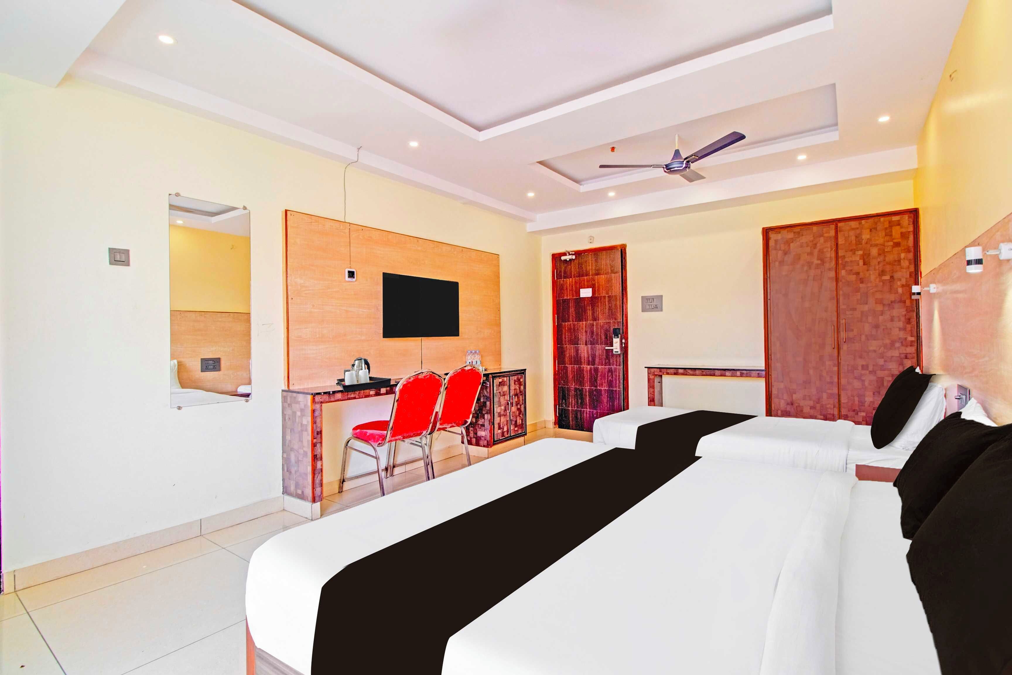 A hotel room with a large bed, a desk with a chair, a television, and a ceiling fan.