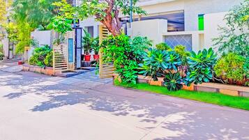 A residential street with modern houses, a gated entrance, and lush greenery.