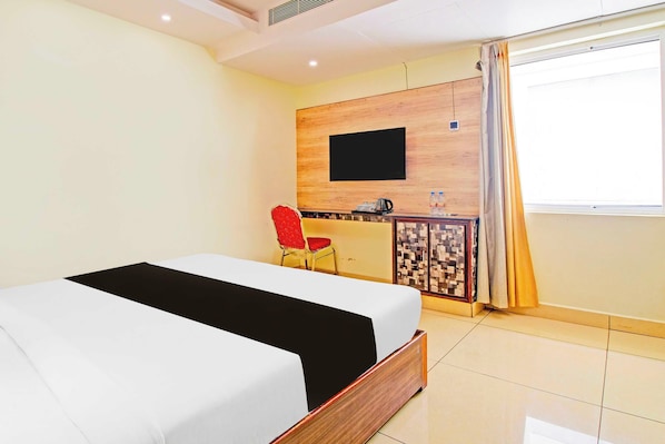 Una habitación de hotel con una cama, un escritorio con silla, un televisor y un ventanal con cortinas.