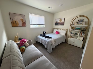 Une chambre à coucher comprenant un lit, une table de chevet, une chaise, une fenêtre, un mur décoré d’œuvres d’art et une bibliothèque.