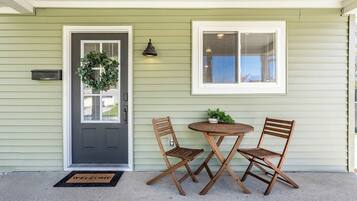 A front door with a wreath, a mailbox, a welcome mat, and two folding chairs with a small table.