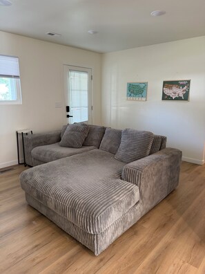 A living room with a large, grey, ribbed sectional sofa, a white door, and two wall-mounted maps.