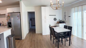 A modern kitchen with a stainless steel refrigerator, wooden flooring, and a dining area with a table and chairs.