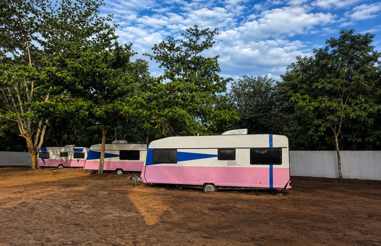 A row of RVs parked in a dirt lot with trees in the background.